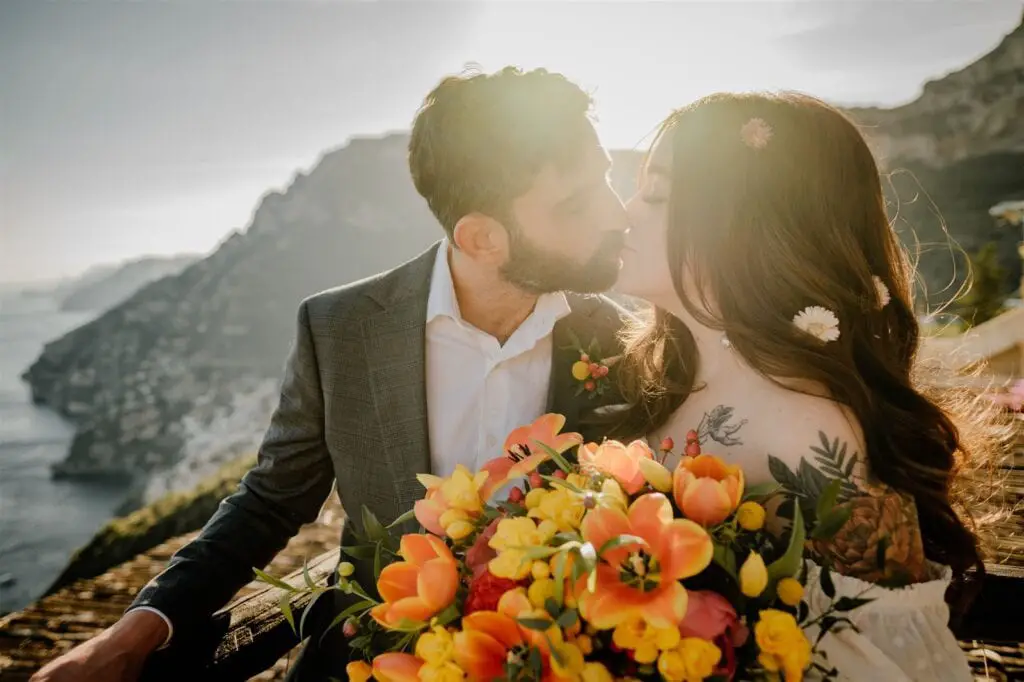 Amalfi Coast Italy elopement bride and groom kiss with the sunset over the ocean and cliffs behind them