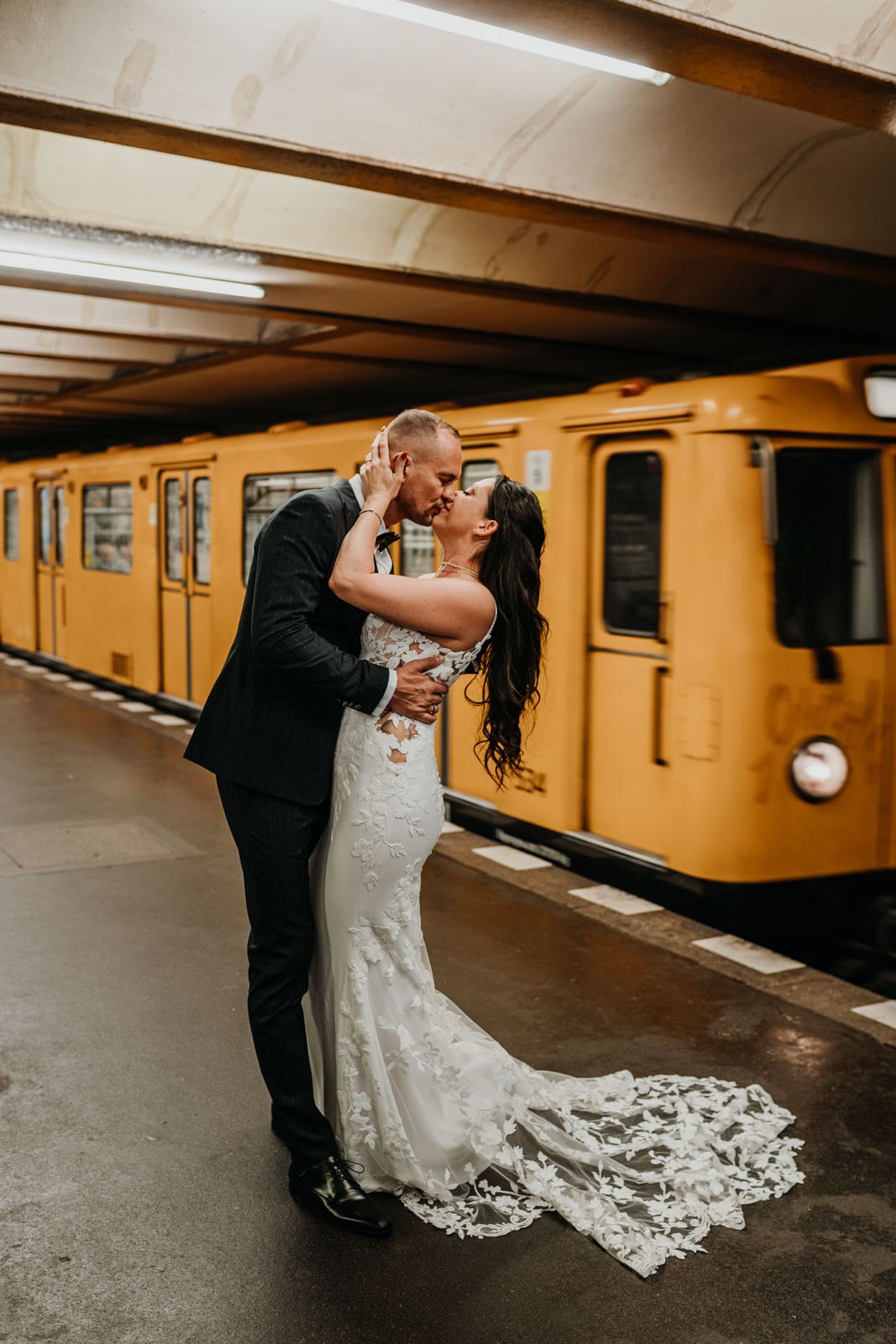 Bride and groom stand on the platform on a subway in Berlin with a yellow train behind them