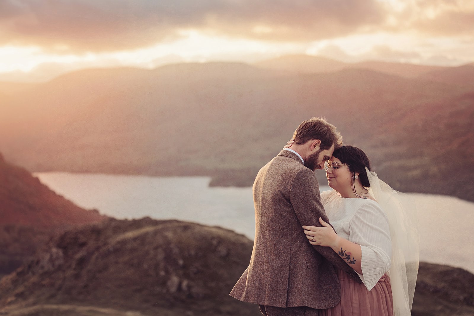 Bride and groom embrace at sunset in Ullswater in Cumbria