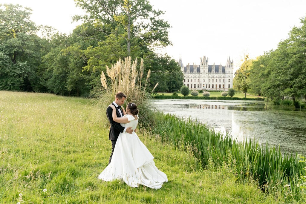 An intimate wedding at Château de Challain in France, bride and groom embrace in the meadows with the castle in the background