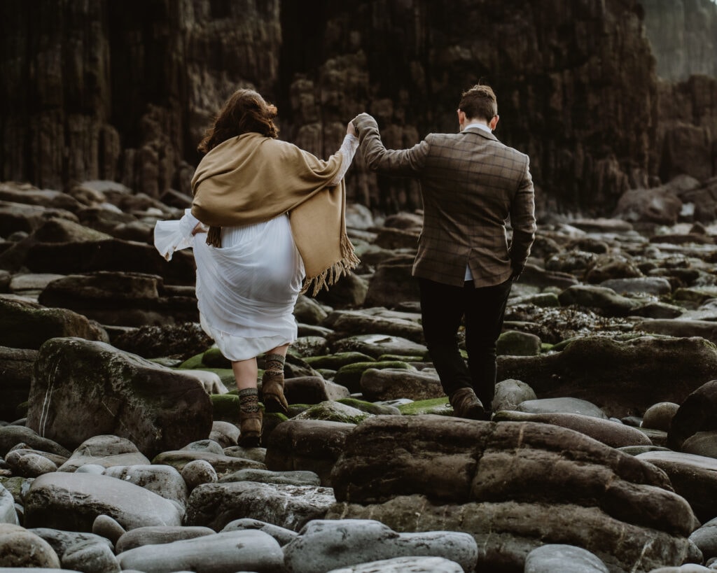 Bride and groom walk hand-in-hand across the beach on the Pembrokeshire coast in Wales