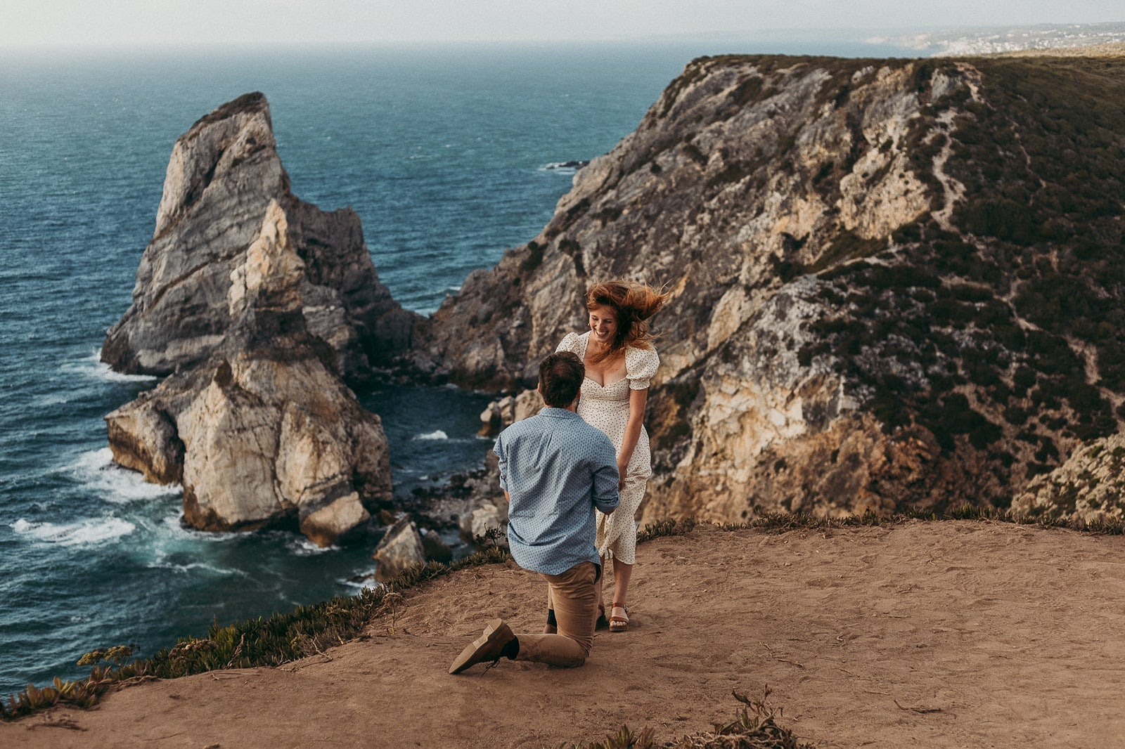 Man down on one knee proposaing to girl on the cliffs of Cabo da Roca in Portugal