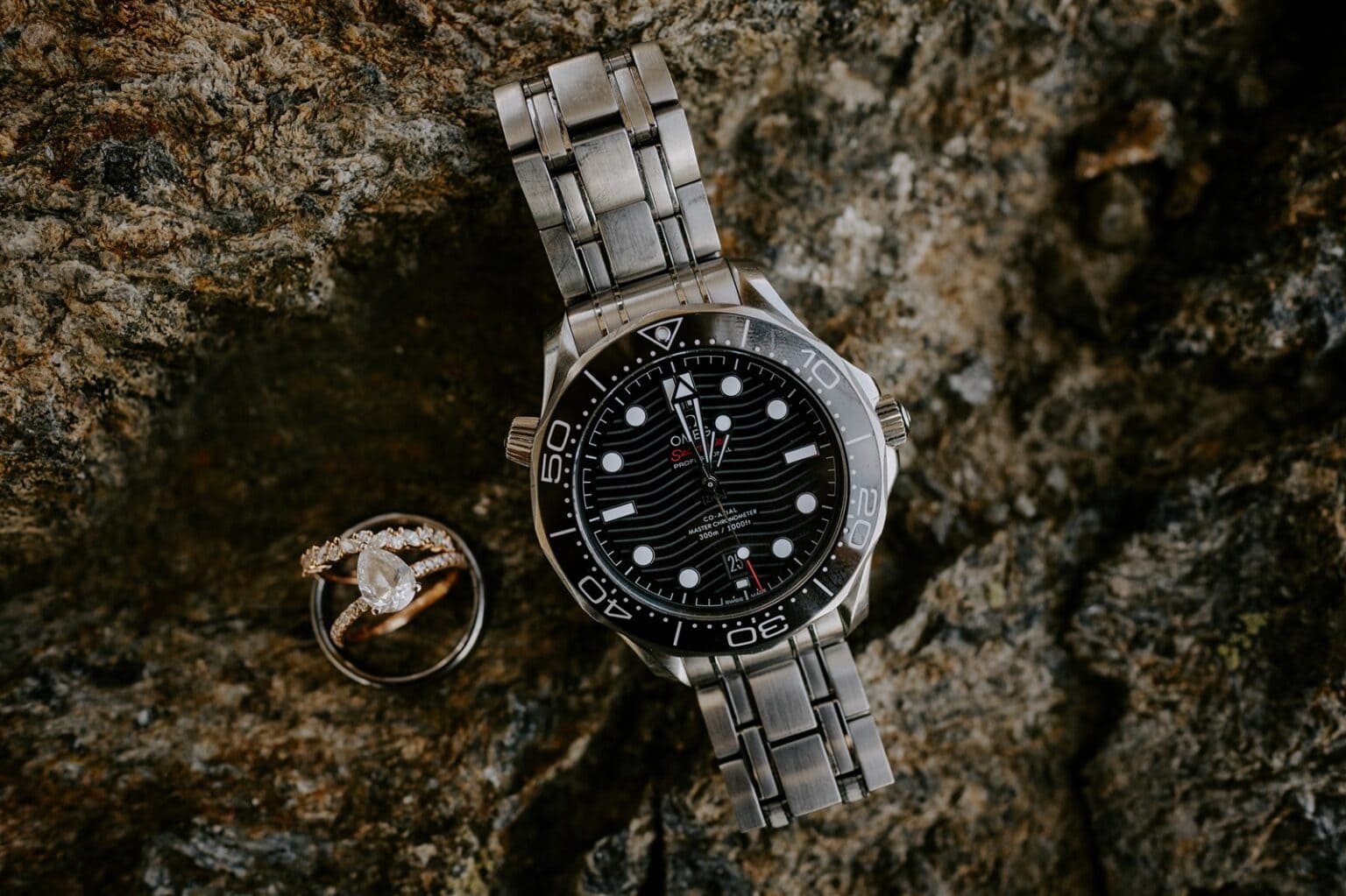 Photos of a watch and wedding rings on a rock