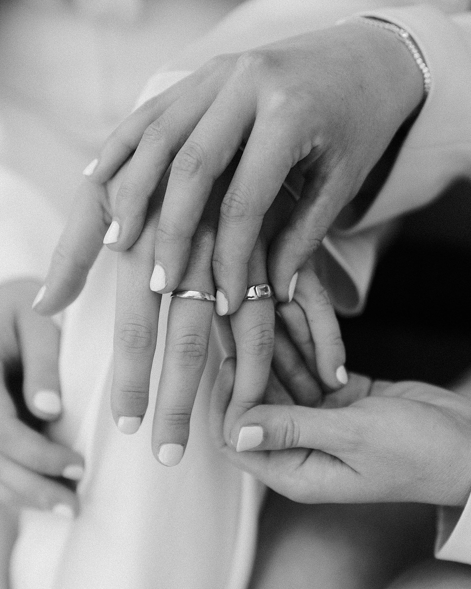 black and white close up image of two hands, showcasing wedding bands.
