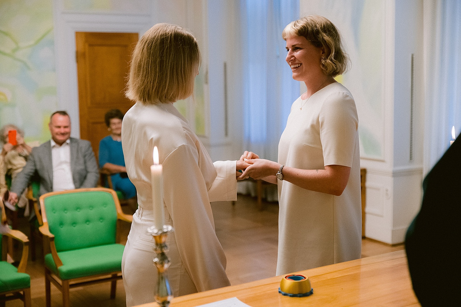 Two brides exchanging wedding rings during their ceremony in City Hall Copenhagen with friends and family sitting behind them.