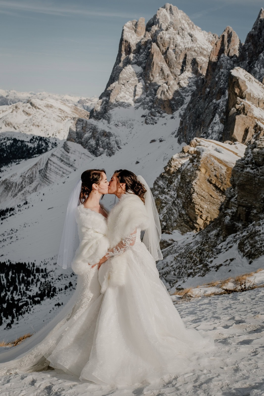 Two brides kissing on a snowy mountain top in the Italian Dolomites
