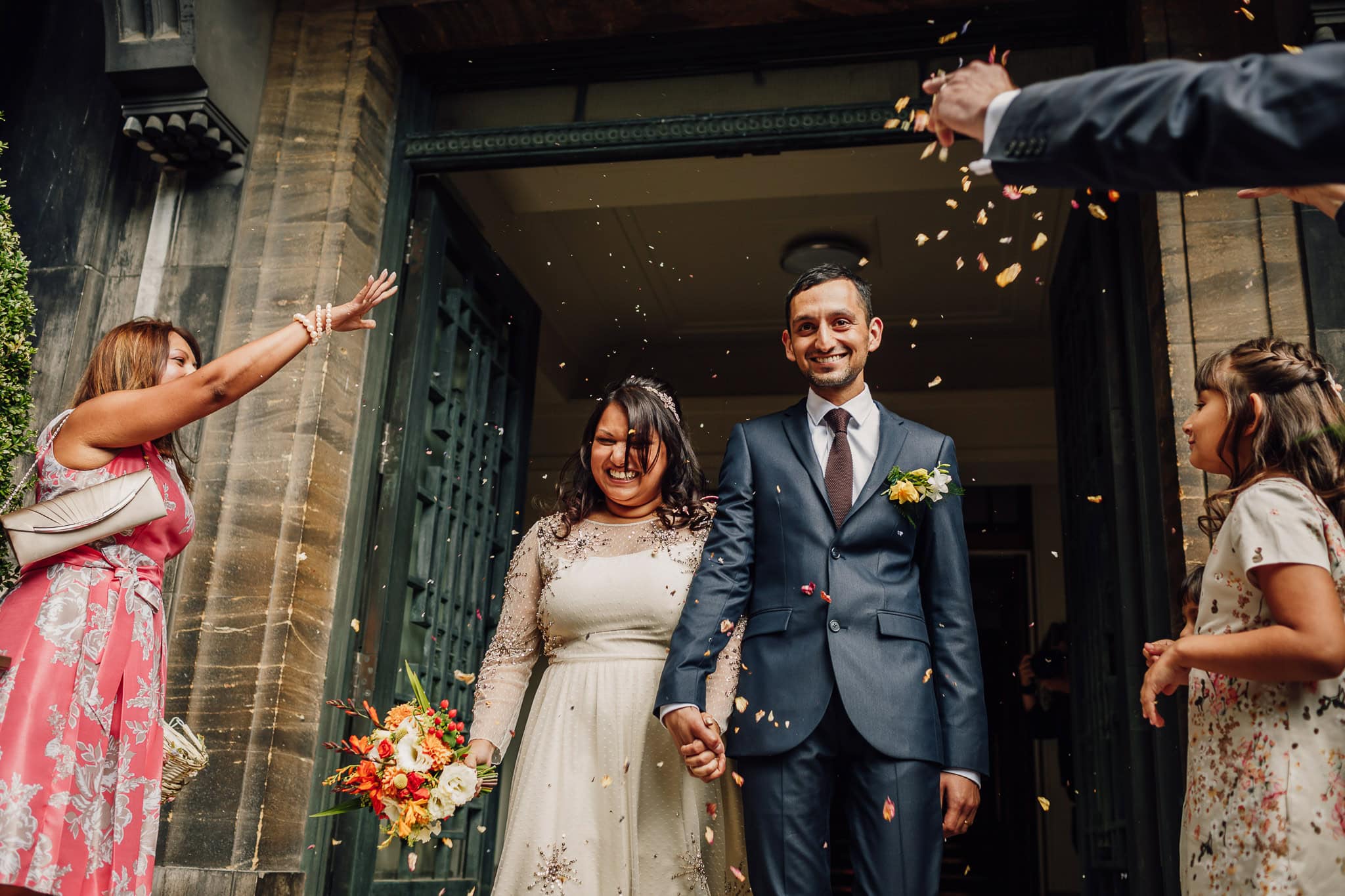 Asian bride and groom leaving Stoke Newington town hall after their registry office ceremony as guests throw confetti over them