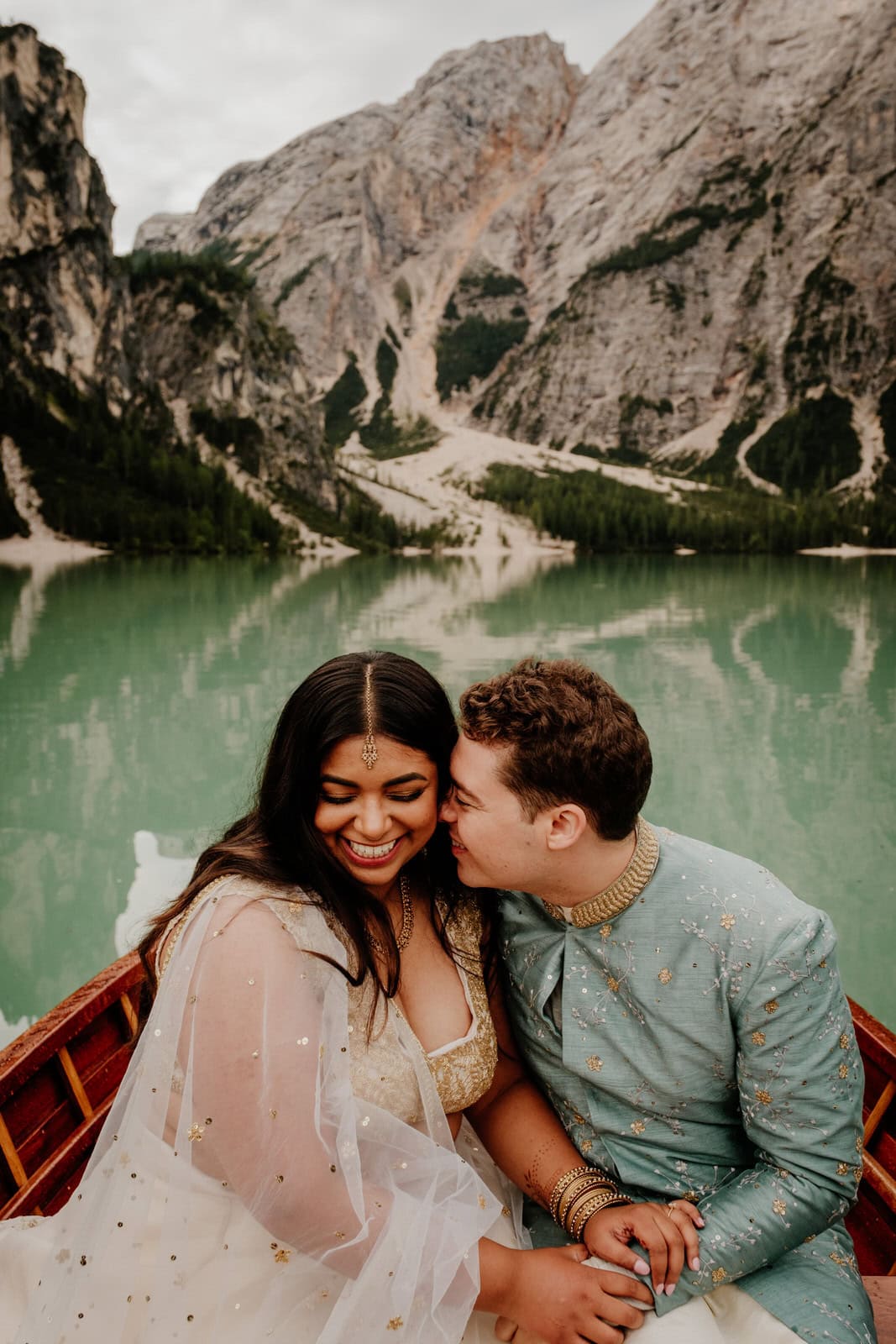 Bride and groom dressed in Indian wedding clothes in a wooden rowing boat on Lake Braies in the Dolomites