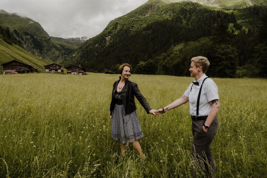 An gender queer, non-binary couple walk throw a grassy meadow. 